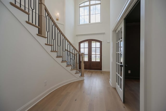 entryway featuring light hardwood / wood-style floors, french doors, and a towering ceiling