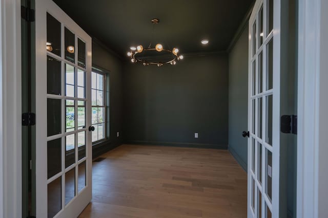 unfurnished dining area with french doors, hardwood / wood-style floors, crown molding, and a notable chandelier