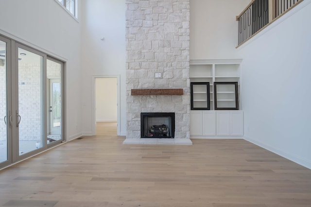 unfurnished living room with a high ceiling, a fireplace, light wood-type flooring, and plenty of natural light