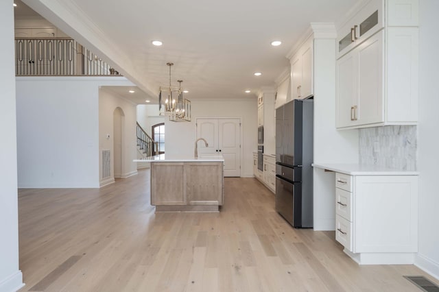 kitchen featuring hanging light fixtures, a center island with sink, backsplash, white cabinetry, and appliances with stainless steel finishes