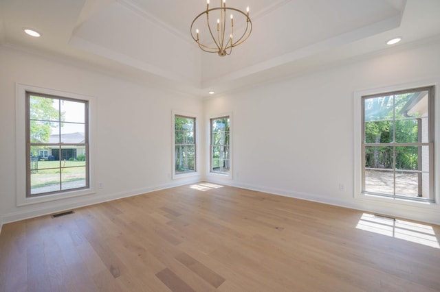 spare room with a raised ceiling, a notable chandelier, crown molding, and light hardwood / wood-style floors