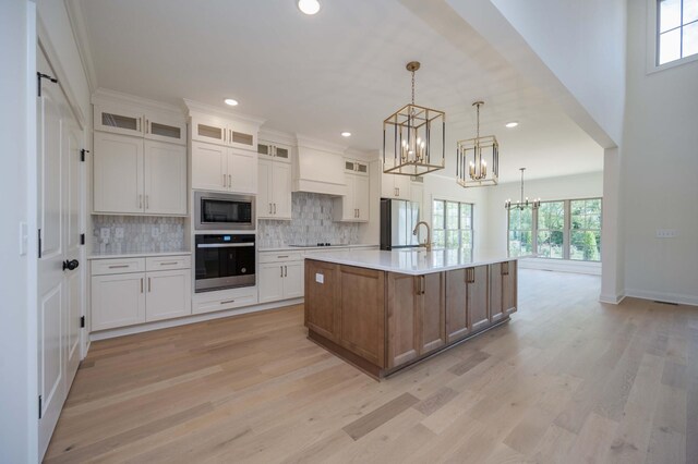 kitchen with appliances with stainless steel finishes, hanging light fixtures, light hardwood / wood-style floors, a large island with sink, and white cabinetry