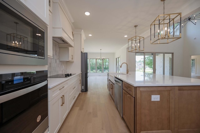 kitchen featuring decorative light fixtures, an island with sink, black appliances, and white cabinetry