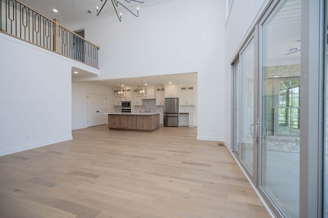 unfurnished living room with a towering ceiling, an inviting chandelier, light wood-type flooring, and ornamental molding