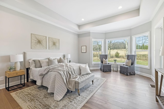 bedroom featuring light hardwood / wood-style floors, crown molding, and a raised ceiling