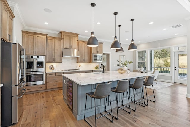 kitchen featuring light stone counters, decorative light fixtures, stainless steel appliances, a breakfast bar area, and a large island with sink