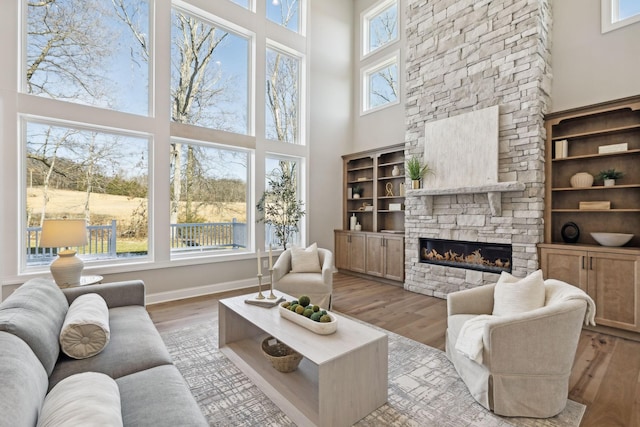 living room featuring light wood-type flooring, a towering ceiling, and a fireplace