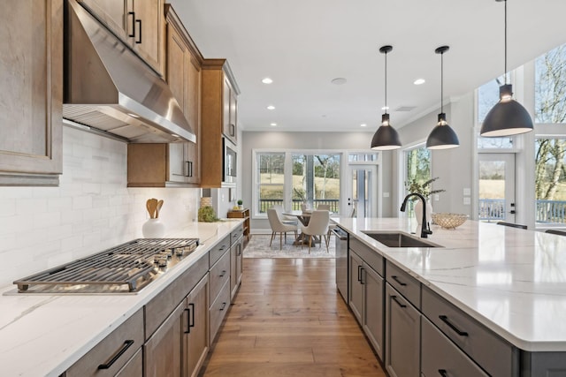 kitchen featuring sink, stainless steel appliances, pendant lighting, backsplash, and a kitchen island with sink