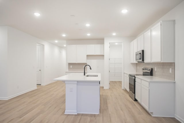 kitchen featuring stainless steel appliances, sink, white cabinets, light wood-type flooring, and an island with sink