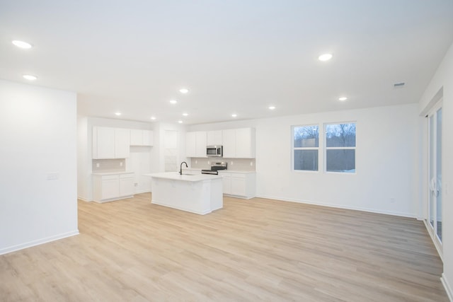 kitchen with sink, white cabinetry, light wood-type flooring, a kitchen island with sink, and appliances with stainless steel finishes