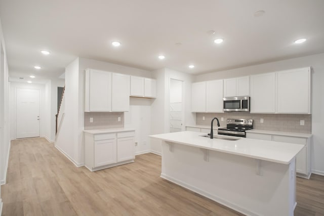 kitchen with appliances with stainless steel finishes, light hardwood / wood-style floors, an island with sink, white cabinets, and sink