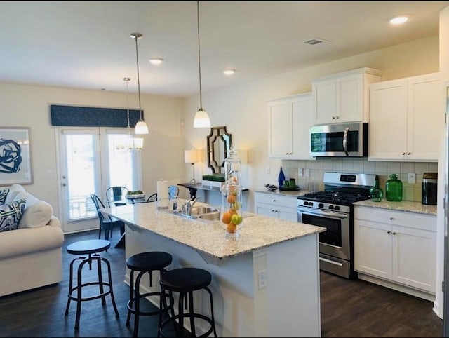 kitchen with white cabinetry, an island with sink, hanging light fixtures, light stone countertops, and appliances with stainless steel finishes