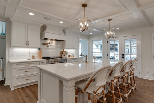 kitchen featuring white cabinets, french doors, custom range hood, an island with sink, and dark hardwood / wood-style flooring