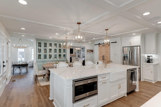 kitchen with a barn door, a center island with sink, stainless steel appliances, sink, and decorative light fixtures