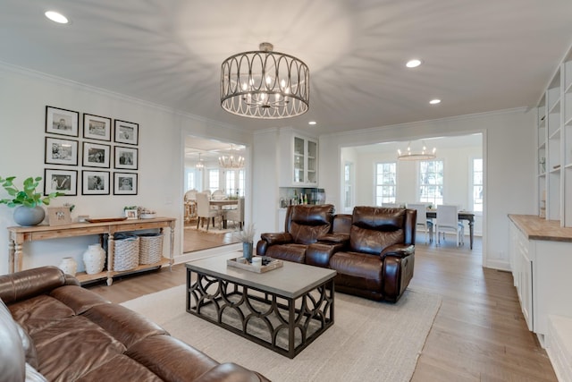 living room featuring an inviting chandelier, built in shelves, crown molding, and light hardwood / wood-style flooring