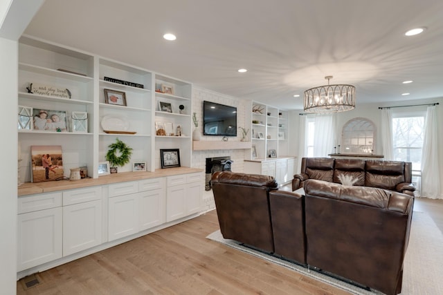 living room featuring a brick fireplace, a chandelier, and light wood-type flooring