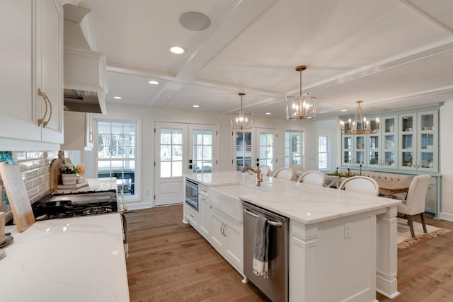 kitchen with a kitchen island with sink, stainless steel appliances, hanging light fixtures, french doors, and white cabinetry