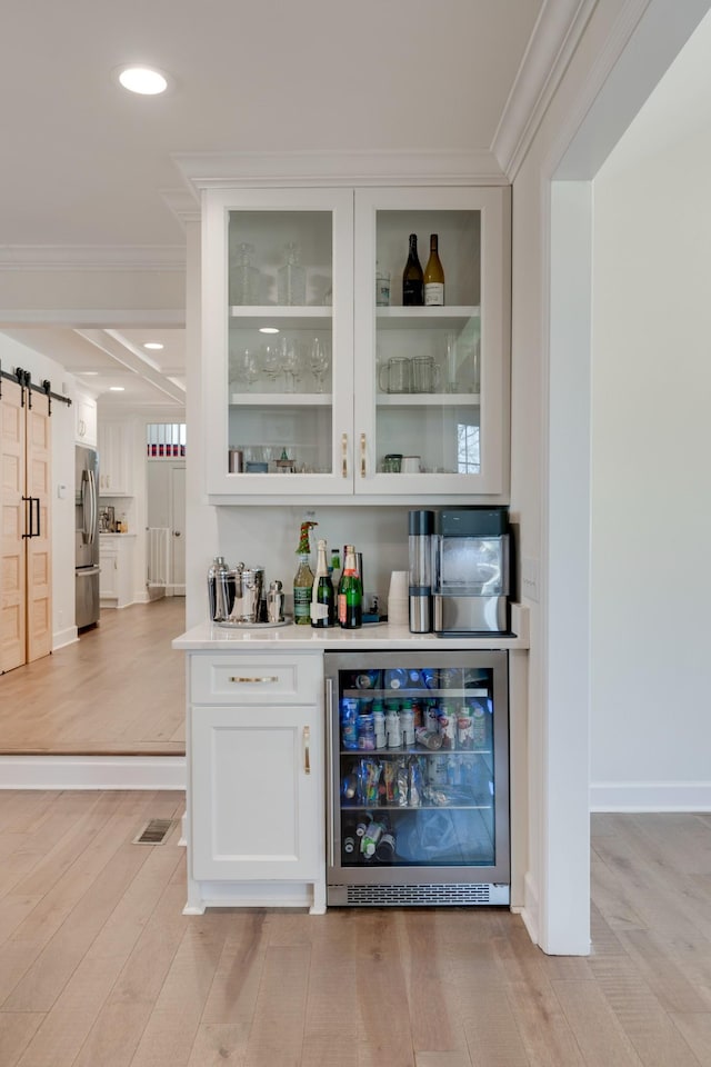 bar featuring stainless steel fridge, light wood-type flooring, a barn door, wine cooler, and white cabinetry