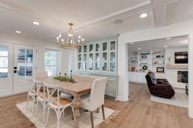 dining area with a chandelier, light hardwood / wood-style floors, a brick fireplace, beam ceiling, and built in features