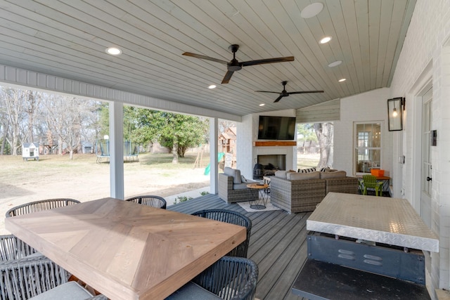 wooden terrace with ceiling fan, an outdoor living space with a fireplace, and a trampoline