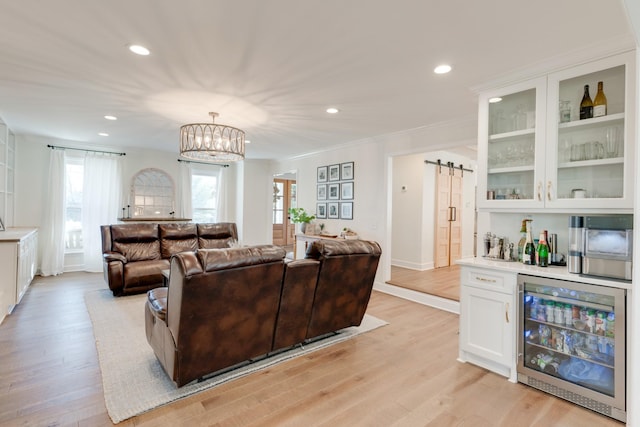 living room featuring beverage cooler, a barn door, ornamental molding, light hardwood / wood-style flooring, and bar area