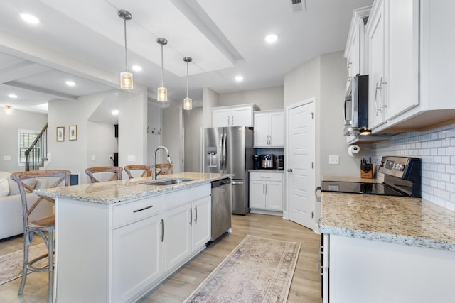 kitchen with hanging light fixtures, stainless steel appliances, tasteful backsplash, a kitchen island with sink, and white cabinets