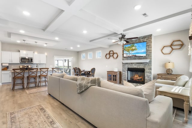 living room with ceiling fan, light hardwood / wood-style flooring, a fireplace, and beam ceiling