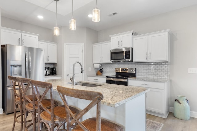 kitchen featuring decorative light fixtures, stainless steel appliances, an island with sink, white cabinetry, and sink