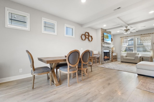 dining space featuring plenty of natural light, light hardwood / wood-style flooring, beamed ceiling, and a stone fireplace