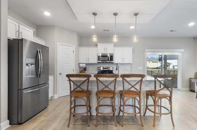 kitchen with appliances with stainless steel finishes, an island with sink, pendant lighting, decorative backsplash, and white cabinets