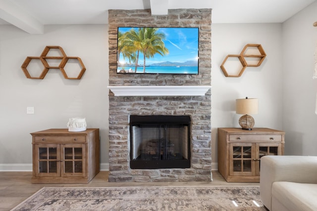 living room with hardwood / wood-style floors, beamed ceiling, and a stone fireplace