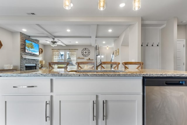 kitchen featuring white cabinets, dishwasher, light stone counters, ceiling fan, and a stone fireplace