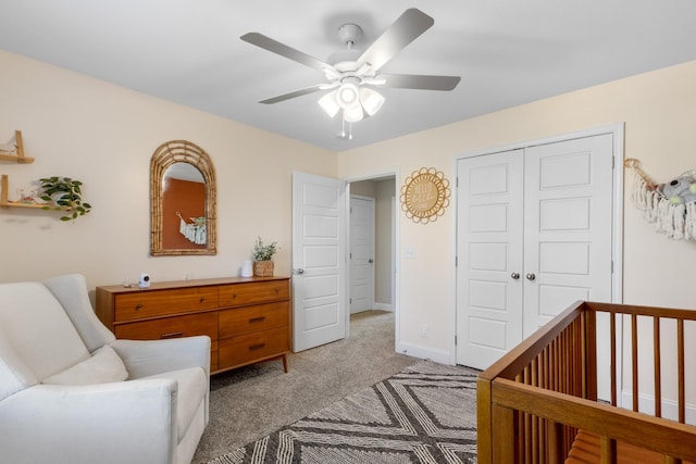 bedroom featuring a closet, ceiling fan, a crib, and light carpet