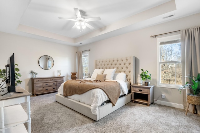 carpeted bedroom featuring a raised ceiling, ceiling fan, and multiple windows