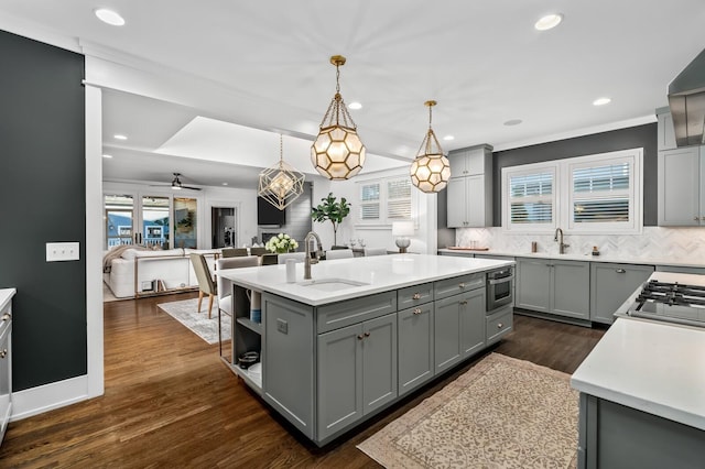 kitchen with sink, pendant lighting, decorative backsplash, gray cabinets, and a kitchen island with sink