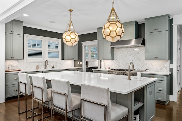 kitchen featuring a center island with sink, decorative light fixtures, wall chimney range hood, and a breakfast bar