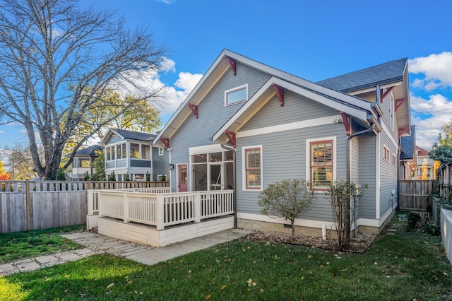 rear view of house with a deck, a lawn, and a sunroom