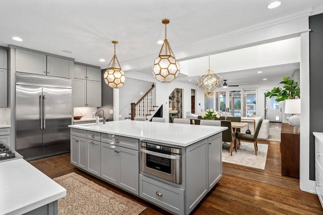 kitchen featuring stainless steel appliances, sink, decorative light fixtures, a center island with sink, and gray cabinetry