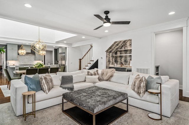 living room featuring ornamental molding, light hardwood / wood-style floors, and ceiling fan with notable chandelier