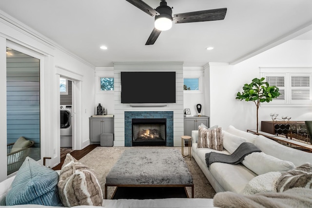 living room with ceiling fan, dark wood-type flooring, ornamental molding, washer / dryer, and a fireplace