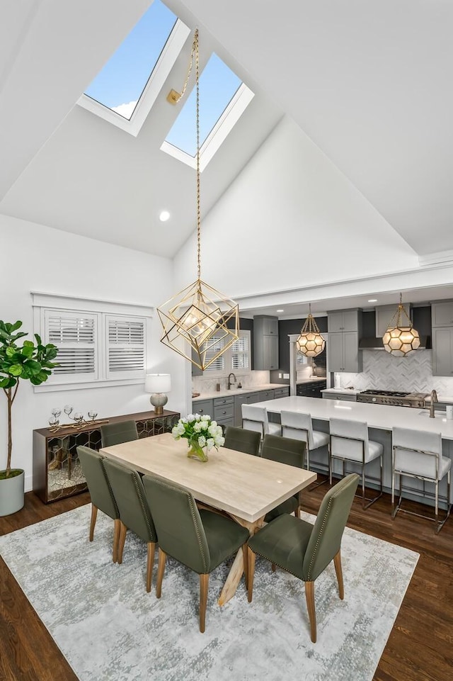 dining space featuring a skylight, dark hardwood / wood-style flooring, high vaulted ceiling, sink, and an inviting chandelier