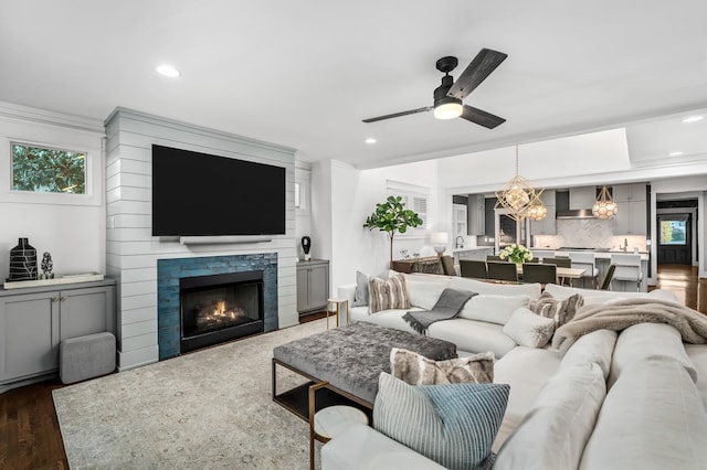 living room with ceiling fan with notable chandelier, a fireplace, a healthy amount of sunlight, and dark wood-type flooring