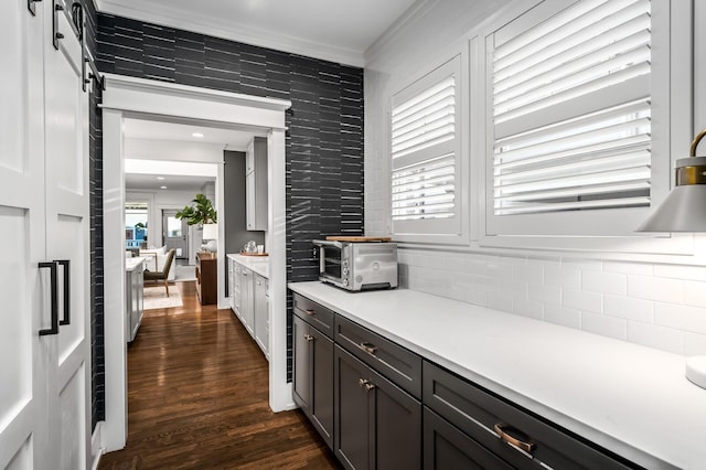 kitchen with decorative backsplash, dark brown cabinets, a barn door, dark hardwood / wood-style flooring, and crown molding