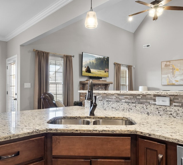 kitchen with sink, vaulted ceiling, light stone counters, ceiling fan, and hanging light fixtures