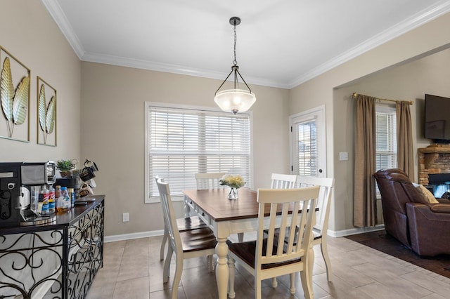 tiled dining space with a healthy amount of sunlight, a stone fireplace, and crown molding