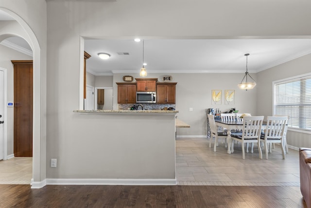 kitchen with hardwood / wood-style flooring, kitchen peninsula, light stone countertops, pendant lighting, and crown molding