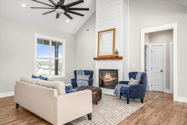 living room with high vaulted ceiling, a large fireplace, ceiling fan, and light hardwood / wood-style flooring