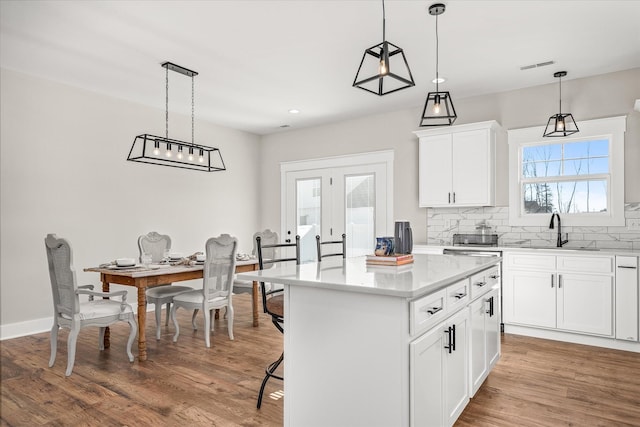 kitchen with visible vents, backsplash, a kitchen island, light wood-type flooring, and a sink