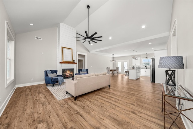 living room with a large fireplace, ceiling fan, light hardwood / wood-style flooring, and vaulted ceiling