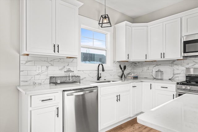 kitchen with a sink, decorative backsplash, appliances with stainless steel finishes, white cabinetry, and decorative light fixtures